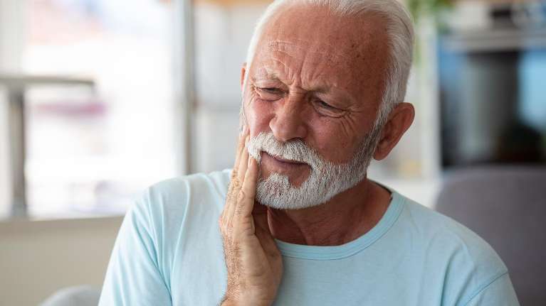Older man holding his jaw in pain, showing symptoms of gum disease or oral discomfort